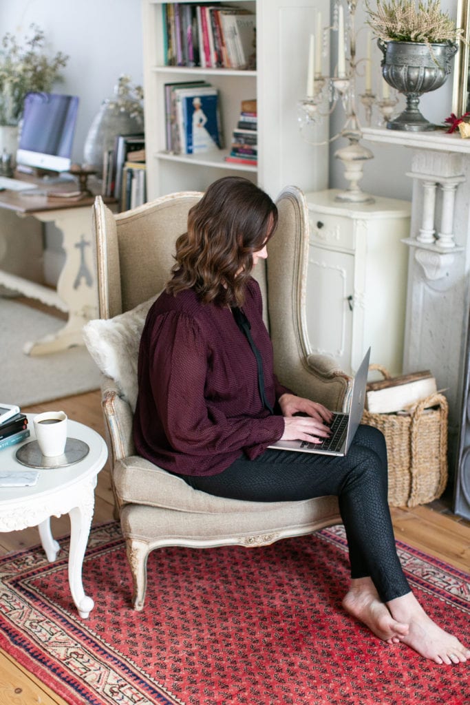 Emma Shard sitting in a high backed antique style chair with her laptop on her lap